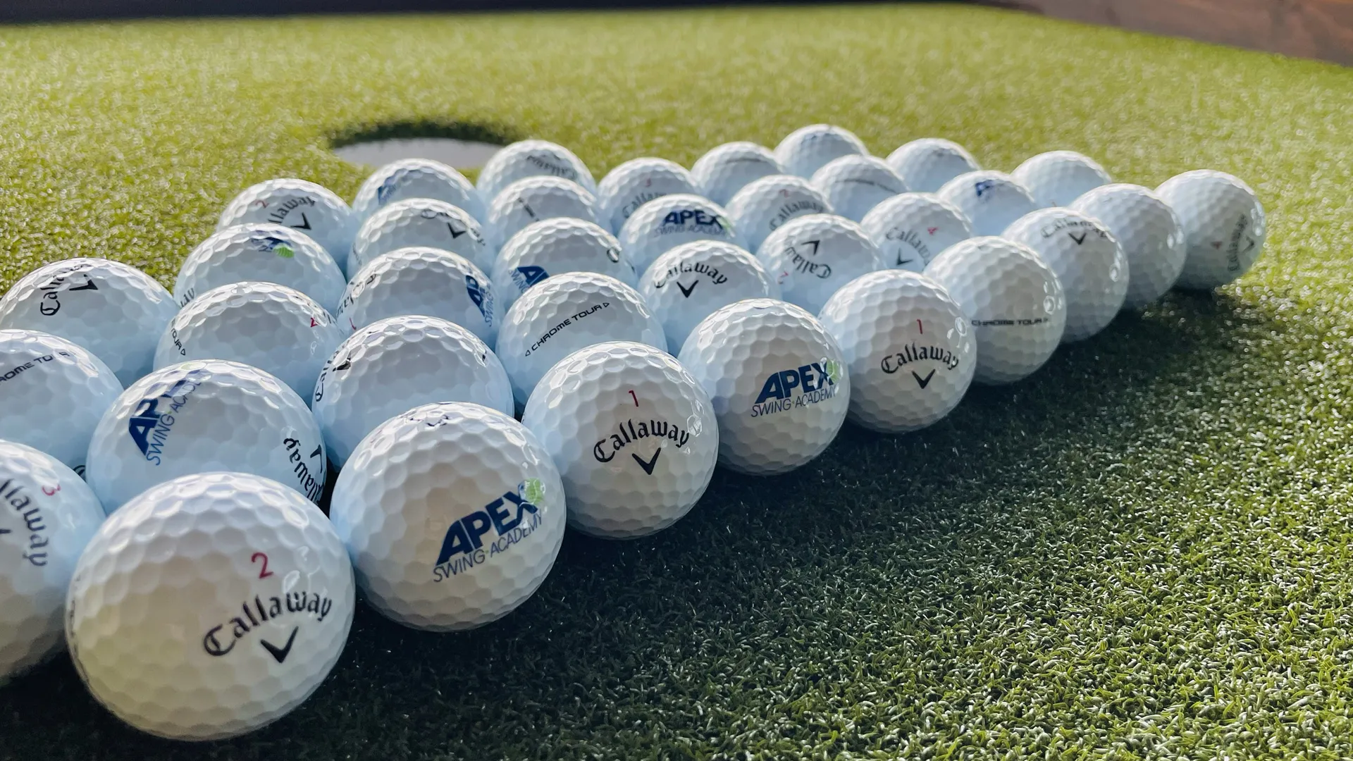 Callaway and APEX branded golf balls on a putting lane at APEX Swing Academy