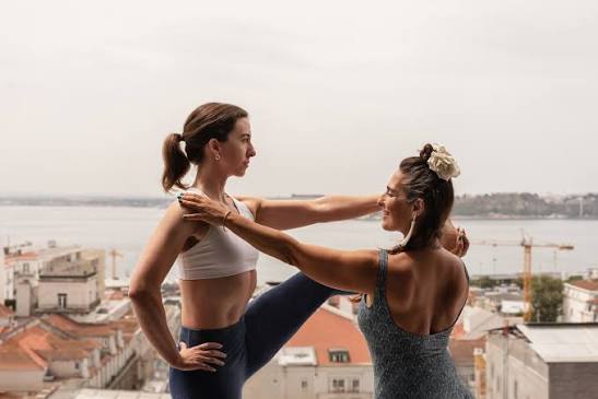 Isa Guitana adjusting a student in a standing pose above the Lisbon rooftops