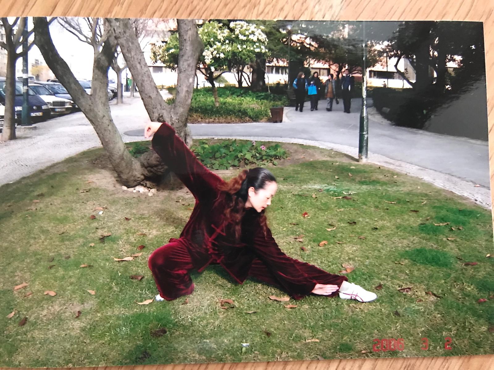 Li Wan, Tai Chi instructor, in a low, flowing Yang style posture on a lawn